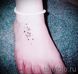 Фото тату маленькой звезды на стопе, окруженной точками. Нежный и минималистичный рисунок.