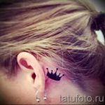 Фото тату: небольшая черная татуировка короны, расположенная за ухом. Простой и элегантный дизайн.