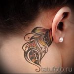 Фото тату красочного пера за ухом. Оригинальный рисунок татуировки с использованием ярких цветов и плавных линий. Идеальный эскиз тату для творческих личностей.