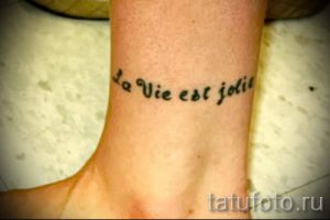Фото тату на лодыжке: черная надпись на французском языке "La Vie est Jolie" (Жизнь прекрасна), выполненная изящным шрифтом.
