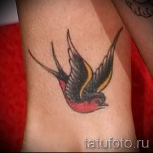 Фото тату ласточки в стиле олд скул на предплечье. Рисунок татуировки выполнен в ярких цветах с использованием красного, желтого и черного.