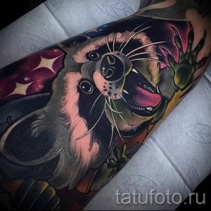 Фото тату енота с открытым ртом на руке. Яркий рисунок с использованием насыщенных цветов и детализированной проработкой.
