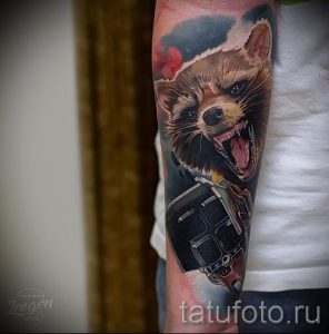 Фото тату енота с фотоаппаратом в стиле нео-трад на предплечье. Яркий рисунок с использованием насыщенных цветов и четких контуров.