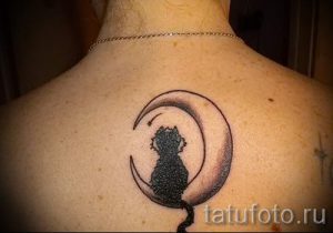 Фото тату: черная татуировка кошки, сидящей на полумесяце, выполнена на спине. Мистический дизайн, детализированная проработка, темные тона.