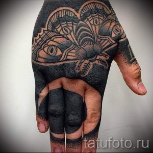 Фото татуировки в стиле трайбл, покрывающей всю ладонь и пальцы. Черно-белый рисунок татуировки с изображением глаз и геометрических фигур.