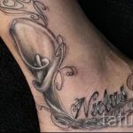 Фото тату: изящная лилия с именем 'Nichole' и датой рождения, выполненная в черно-серых тонах на лодыжке.