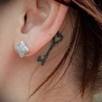 Фото тату ключа с сердцем на конце за ухом. Черный контур, минималистичный стиль, символ любви и секретов, эскиз тату.