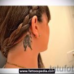 Фото тату: изящное перо на затылке девушки с заплетенной косой. Черно-серый рисунок татуировки с детализированной проработкой.