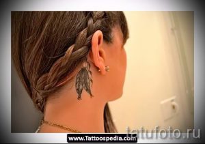 Фото тату: изящное перо на затылке девушки с заплетенной косой. Черно-серый рисунок татуировки с детализированной проработкой.