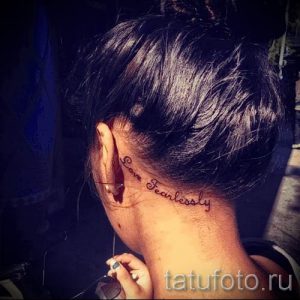 Фото тату надписи 'Love Fearlessly' за ухом. Черный контур, минималистичный стиль, женственная татуировка, вдохновляющий девиз, эскиз тату.