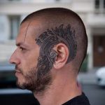 Фото тату: большая татуировка с изображением дракона на затылке и части головы у мужчины. Детализированный рисунок татуировки в стиле ориентал.