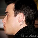 Фото тату: красивая заглавная буква 'B' на затылке у мужчины. Каллиграфический рисунок татуировки, выполненный с плавными линиями.