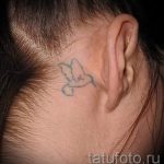 Фотография простой татуировки птицы, выполненной в сером цвете на затылке. Небольшой рисунок татуировки для тех, кто ценит лаконичность.