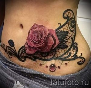 Фото тату: красивая роза, окруженная черным кружевом, на животе. Идея для женской татуировки в стиле blackwork и акварель.