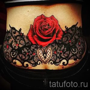 Фото тату: татуировка на животе, сочетающая в себе кружевой узор и красную розу. Рисунок выполнен в реалистичном стиле с добавлением ярких акцентов.