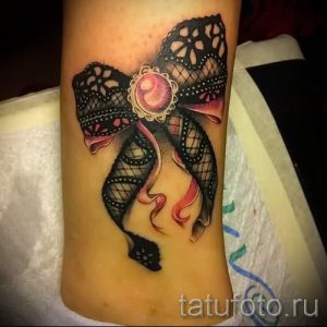 Фото тату: цветная татуировка с изображением кружевного банта и розы на женской руке. Детализированный рисунок с акцентом на текстуру и цветовые переходы.