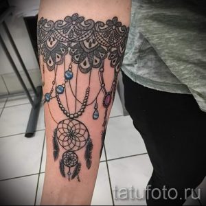 Фото тату: Черно-серая татуировка на руке, изображающая кружево, ловец снов и бусины. Детализированный рисунок с использованием различных текстур.