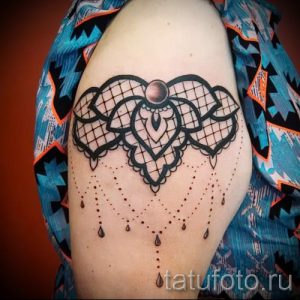 Фото тату: Черно-серая кружевная татуировка на плече, выполненная в технике графики. Детализированный рисунок кружева с каплевидными элементами.