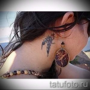 Фото тату с изображением ловца снов и пера на задней части шеи. Рисунок татуировки выполнен в черно-серых тонах с добавлением коричневых акцентов.