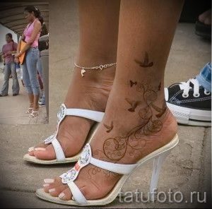 Фото тату: красивая татуировка на лодыжке с изображением летящих птиц, цветочных узоров и геометрических элементов, выполненная в черно-коричневой гамме.