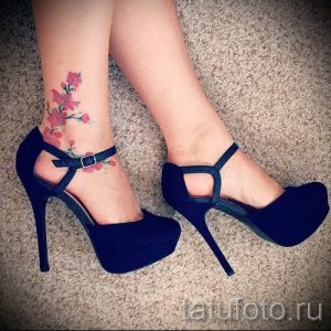 Фото тату цветущей сакуры на лодыжке и стопе. Цветная татуировка с розовыми и зелеными оттенками.