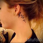Фото татуировки: музыкальная композиция из нот и скрипичного ключа на затылке, выполненная в черном цвете.