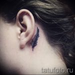 Фото тату: маленькое черное перо, выполненное в технике лайнарт, расположено за ухом. Нежный и изящный рисунок татуировки для девушек.