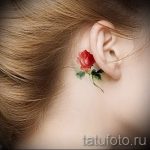 Фото тату: маленькая красная роза, расположенная за ухом. Детализированный и реалистичный рисунок татуировки.