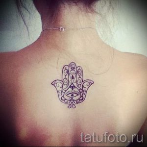 Фото тату Хамса на шее девушки. Черно-белый рисунок с детальной проработкой узоров и выразительным глазом в центре ладони.