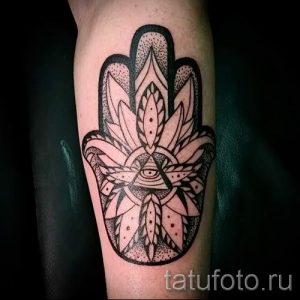 Фотография черно-белой татуировки Хамса на предплечье, выполненной в технике графика с использованием точечных узоров и четких линий.