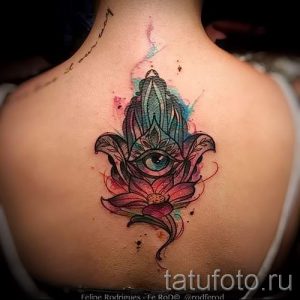 Фотография цветной татуировки Хамса на спине, выполненной в акварельной технике с использованием розовых, синих и зеленых оттенков.