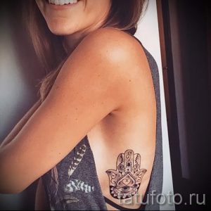 Фото тату: черная татуировка в виде руки Хамса с детальным орнаментом на боку девушки.
