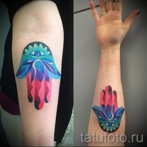 Фото яркой акварельной татуировки Хамса на руке. Рисунок выполнен в различных цветах и оттенках, создавая эффект размытости и легкости.