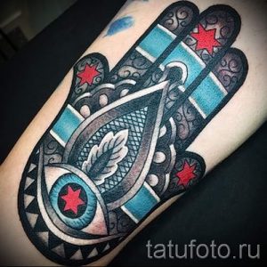 Фото цветной татуировки Хамсы на предплечье. Рисунок татуировки выполнен в ярких цветах с использованием бирюзового, красного и черного.