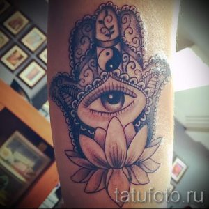 Фото татуировки Хамса (Рука Фатимы) на предплечье. Изображение выполнено в ярких цветах с детальной проработкой узора и добавлением символов Инь-Янь и лотоса.