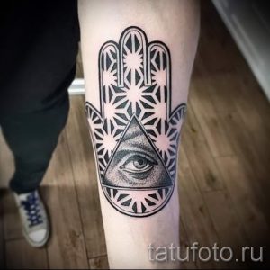 Фото татуировки Хамса (Рука Фатимы) на колене. Изображение выполнено в черном цвете с использованием геометрических узоров и треугольника с глазом.