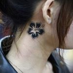 Фото тату: маленький цветок гибискуса, расположенный за ухом. Изящный и женственный рисунок татуировки в черном цвете.