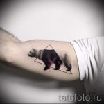 Фото тату медведя в геометрическом треугольнике на предплечье. Черно-серый рисунок татуировки с детальной проработкой шерсти и минималистичным дизайном.
