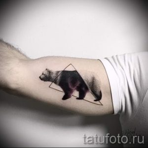 Фото тату медведя в геометрическом треугольнике на предплечье. Черно-серый рисунок татуировки с детальной проработкой шерсти и минималистичным дизайном.