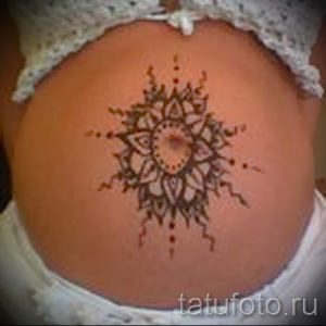 Фото менди на животе: сложный восточный узор, выполненный хной. Круглая композиция с мелкими деталями и тонкими линиями. Коричневый рисунок татуировки на светлой коже.
