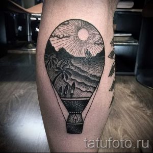 Фото тату на ноге: воздушный шар, внутри которого изображен горный пейзаж с солнцем и пальмами. Черно-белый рисунок татуировки в графичном стиле.