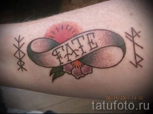 Фото татуировки на предплечье: лента с надписью 'FATE', украшенная розой и окруженная руническими символами. Эскиз татуировки выполнен в традиционном стиле.