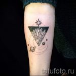 Фото татуировки на предплечье: черный треугольник с кристаллами внутри, планеты и солнце. Минималистичный дизайн, точечные линии.