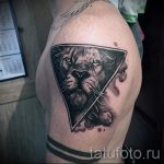 Фото тату: треугольник с изображением головы льва, расположенный на плече. Реалистичный рисунок татуировки в черно-белом стиле с использованием теней.