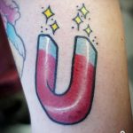 Фото тату подковы с оранжевыми молниями на руке. Традиционный рисунок татуировки в стиле олдскул с четкими контурами и яркими цветами.