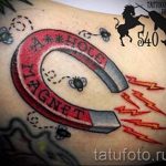 Фото тату подковы с оранжевыми молниями, мухами и надписью "A HOLE MAGNET" на руке. Стильный рисунок татуировки в стиле олдскул с использованием ярких цветов.