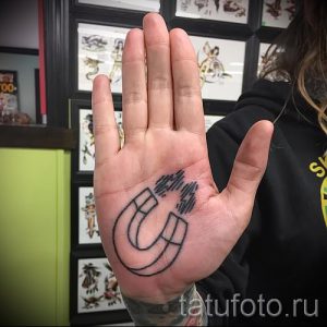 Фото тату подковы на ладони. Простой и лаконичный рисунок татуировки в стиле минимализм, выполненный тонкими черными линиями.