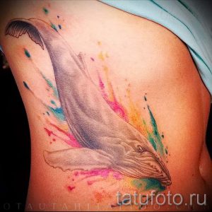 Фото акварельной татуировки кита на боку. Разноцветные брызги краски и нежные линии создают яркий и запоминающийся образ.