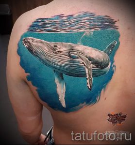 Фото реалистичной татуировки кита, плывущего под водой на спине. Детализированное изображение с использованием ярких цветов и теней.