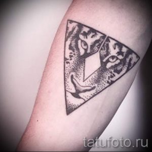 Фото татуировки на руке с изображением треугольника, внутри которого находится стилизованная кошачья морда. Рисунок выполнен в черно-белом цвете.
